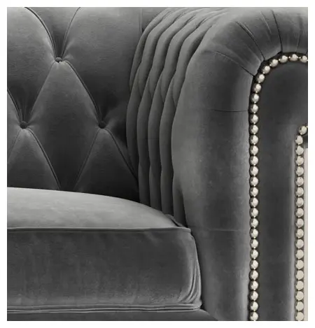 Close-up of a grey tufted armchair with pleated details and silver stud accents.