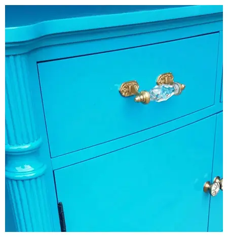 A close-up of a bright blue cabinet with ornate gold and crystal knobs.