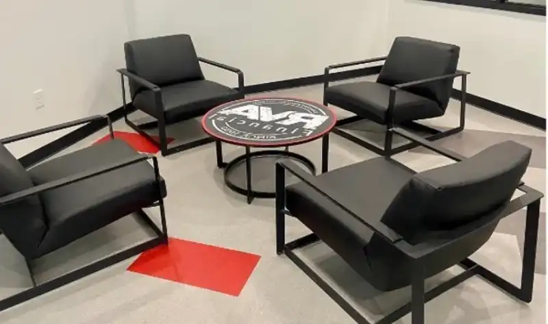 Four black chairs arranged around a round table with a sports team logo in a modern waiting room setting.