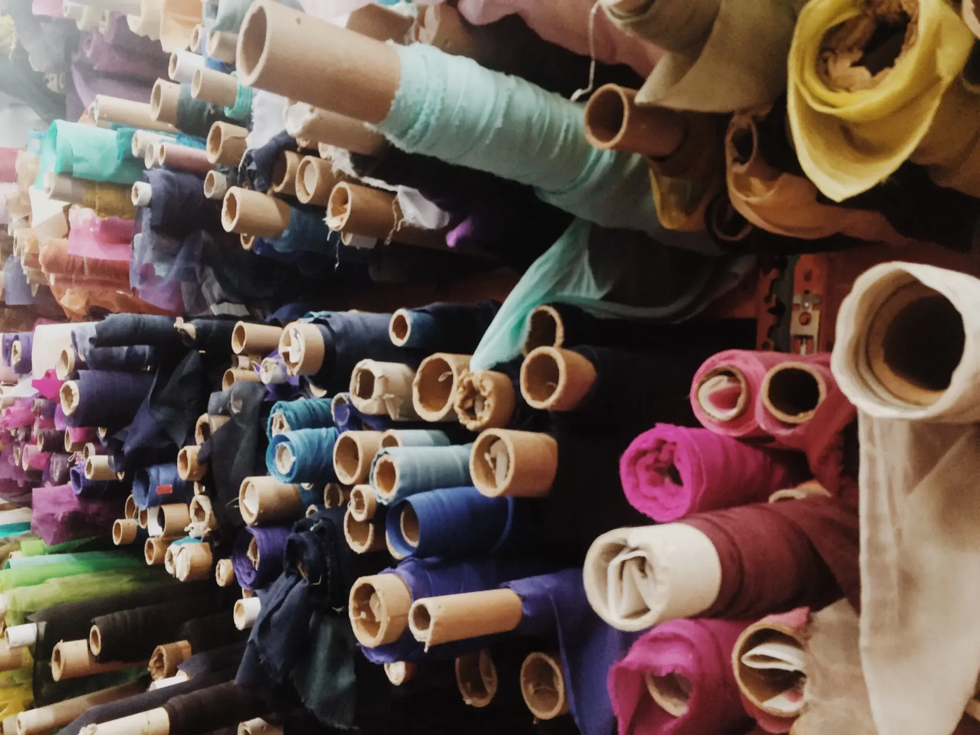 Rows of colorful fabric rolls arranged horizontally on shelves, showcasing a variety of colors and textures.