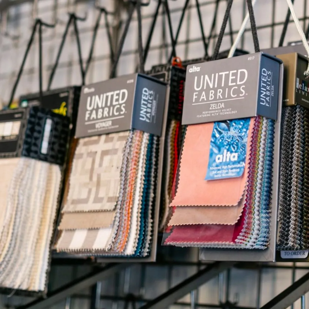 Fabric swatches in various colors and patterns hang from display racks in a store, labeled with different brand names.