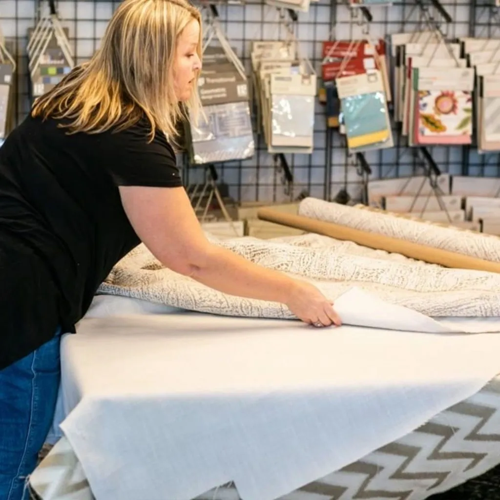 A woman measuring fabric on a table in a craft store.