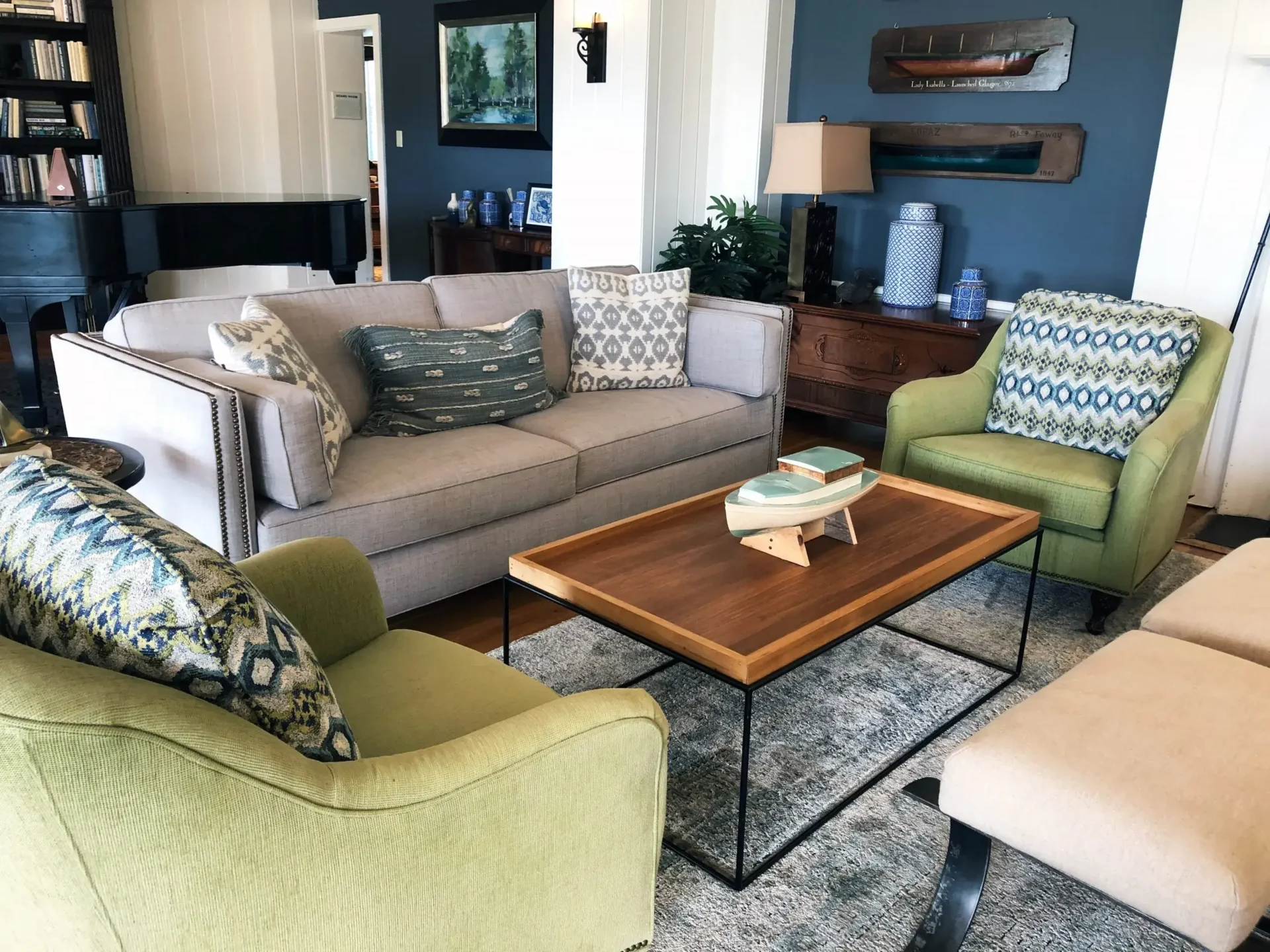 A well-decorated living room with a beige sofa, two green armchairs, a wooden coffee table, and nautical decor.